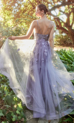 A woman stands outdoors among greenery, gracefully holding her Floral-Embroidered Long A-Line Prom Gown A1191, which features thin straps and a flowing silhouette.