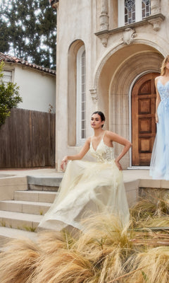 A woman in a Floral-Embroidered Long A-Line Prom Gown A1191 sits on stone steps outside a building with an arched doorway and tall windows.
