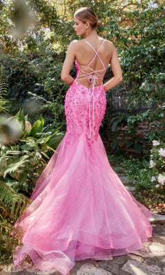 Outdoors in a garden, a woman wears the Floral Beaded Long Mermaid Prom Dress A1201, featuring bright pink fabric, a lace-up open back, 3-D floral appliques, and stunning floor-length detail.