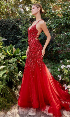 A woman stands outdoors in a garden, wearing the Floral Beaded Long Mermaid Prom Dress A1201, a fitted, floor-length red gown featuring sparkling embellishments and lace-up sides.