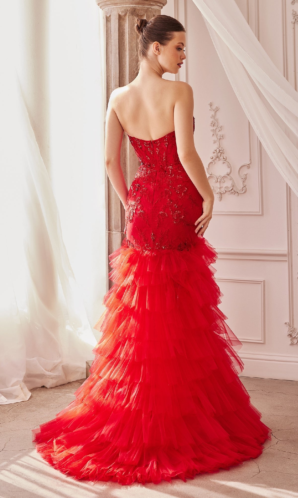 A woman stands indoors, facing away, wearing the Strapless Fitted Ruffle Prom Dress A1255 featuring a mermaid silhouette with lace details and a dramatic ruffle tulle skirt.