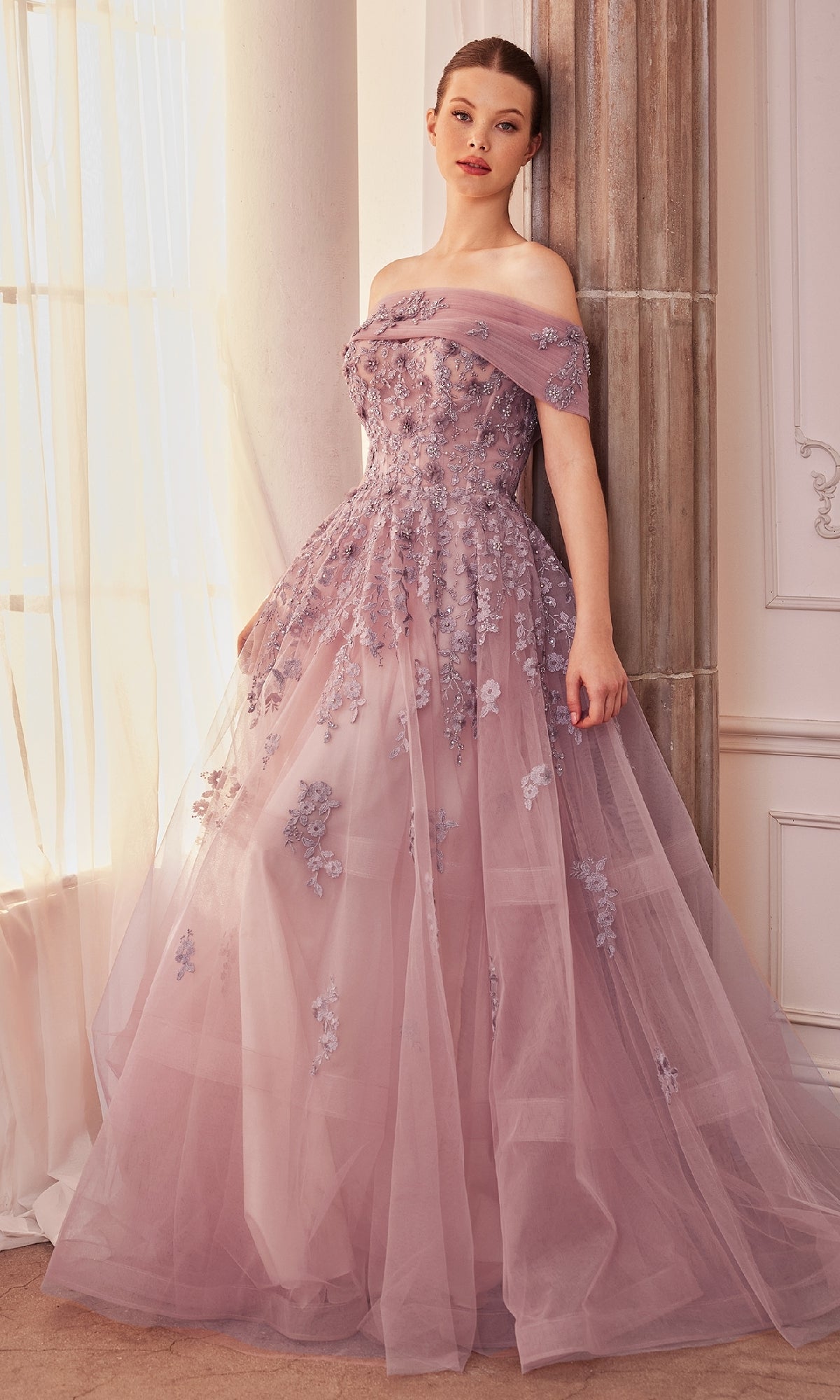 A woman stands by a window and column in a refined room, wearing the Long Strapless Sweetheart A-Line Prom Dress A1348, a floor-length gown featuring elegant floral appliqués.
