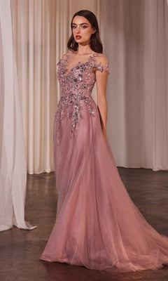 A woman poses in the Andrea and Leo A1350 Dusty Rose Prom Ball Gown, featuring a floor-length off-the-shoulder design with floral embroidery and sheer tulle overlay, set before light curtains.