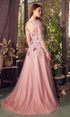 A woman stands indoors in front of a window, wearing the Andrea and Leo A1356 long formal pink dress with floral sequin embroidery, sheer sleeves, and an elegant A-line skirt, slightly turned to show its graceful back design.