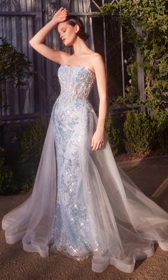 A woman stands outdoors in the sunlight, wearing the Andrea & Leo A1365 strapless sequin prom gown, featuring light blue embroidery and a sheer train.