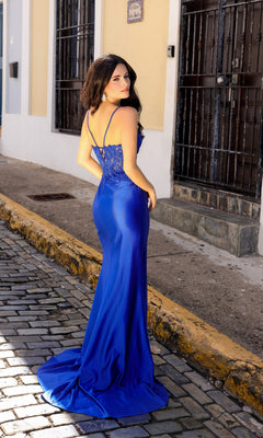 A woman in the Long Sweetheart Prom Dress with Sheer Corset A1374, a fitted, floor-length royal blue gown with a sheer corset bodice, stands on a cobblestone street and looks over her shoulder at the camera.