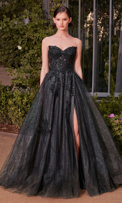 A woman stands outdoors in the Andrea & Leo A1378 strapless long prom dress, featuring a corset-style waist, glittery black fabric, embroidered floral lace accents, and a thigh-high slit.