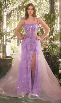 A woman stands indoors in the Long Glitter Prom Dress: Andrea and Leo A1382, a sheer lavender lace-up gown with a high slit and sparkling details, surrounded by potted plants and natural light.