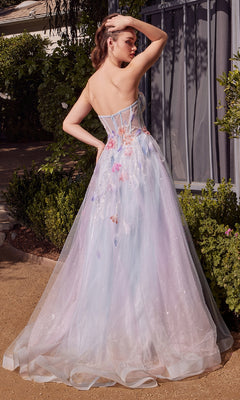A woman stands outdoors in the Andrea & Leo A1383 long strapless prom dress, featuring glitter, floral details, and a sheer corset back, surrounded by greenery and sunlight.