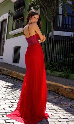 A woman in the Sheer-Corset Long Prom Dress with Side Train A1384 stands on a cobblestone street outdoors, near green and white buildings, looking over her shoulder and wearing drop earrings.