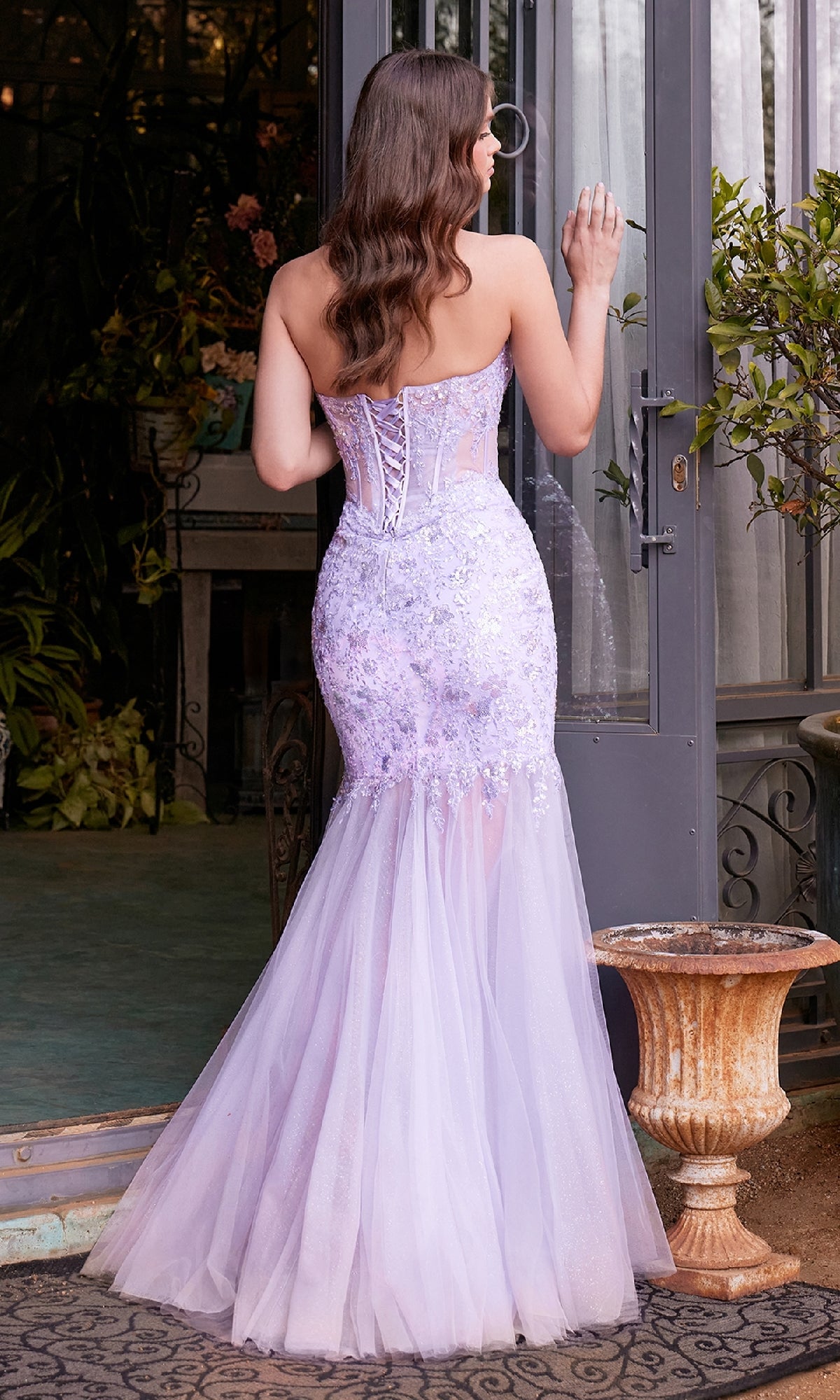 A woman wearing the Strapless Mermaid Prom Dress: Andrea & Leo A1388 stands with her back to the camera, facing an open glass door.