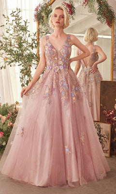 A woman in the Mauve Pink Long Prom Ball Gown (CLA1394), featuring floral-lace appliques, stands before a mirror amid lush greenery and blooming flowers.