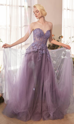 A woman in the Andrea & Leo A1398 strapless glitter prom gown poses holding her dress in a sunlit room with sheer curtains and floral accents.