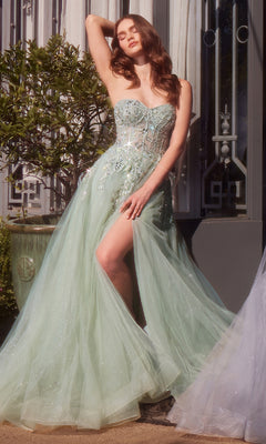 A woman in a sheer, light green Strapless Prom Ball Gown: Andrea & Leo A1415 with floral embellishments stands outdoors, posing with one arm raised and revealing one leg through a thigh-high slit.