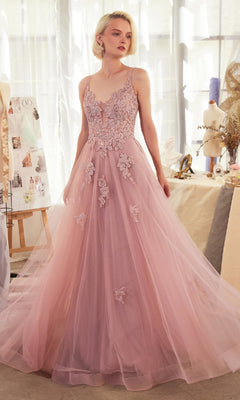 A woman stands in a bright studio, surrounded by mannequins and sketches, wearing the Andrea & Leo A1417 blush pink embroidered long prom dress with a tulle skirt.