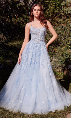 A woman stands outdoors in the Andrea and Leo A1437 long blue prom ball gown, featuring floral embroidery and a tulle skirt that beautifully complements the surrounding green foliage and grass.