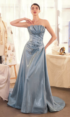 A woman stands indoors wearing the Andrea & Leo A1439 long prom dress, a strapless blue A-line gown in shiny liquid satin with draped detailing.
