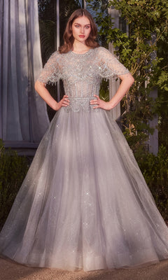 A woman stands outdoors wearing the Andrea and Leo A1444 long formal dress, featuring silver glitter fabric, sheer short sleeves, a beaded bodice, and an elegant A-line skirt, with her hands confidently on her hips.