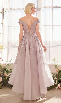 A woman wears the Andrea and Leo A1454 long prom dress featuring pastel tones, floral embroidery, and a lace-up back, standing before sheer curtains and floral decorations.