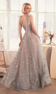A woman in the Andrea & Leo A1458 long silver prom ball gown stands in a softly lit room, looking over her shoulder.