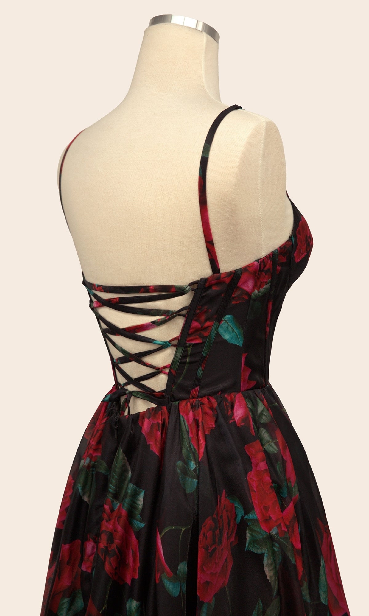 A mannequin showcases the Andrea & Leo A1465 long floral-print prom dress, featuring a sleeveless design, black lace-up back, and bold red rose pattern.