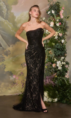 A woman wearing the black Andrea and Leo A1497 long prom dress stands with hands on hips in front of a floral arrangement and painted backdrop.