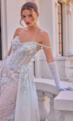 A woman wears the Ethereal Blue Prom Dress: Andrea & Leo A1518, a light blue, beaded, off-the-shoulder corset gown with floral embroidery, sequins, and matching sheer opera gloves.