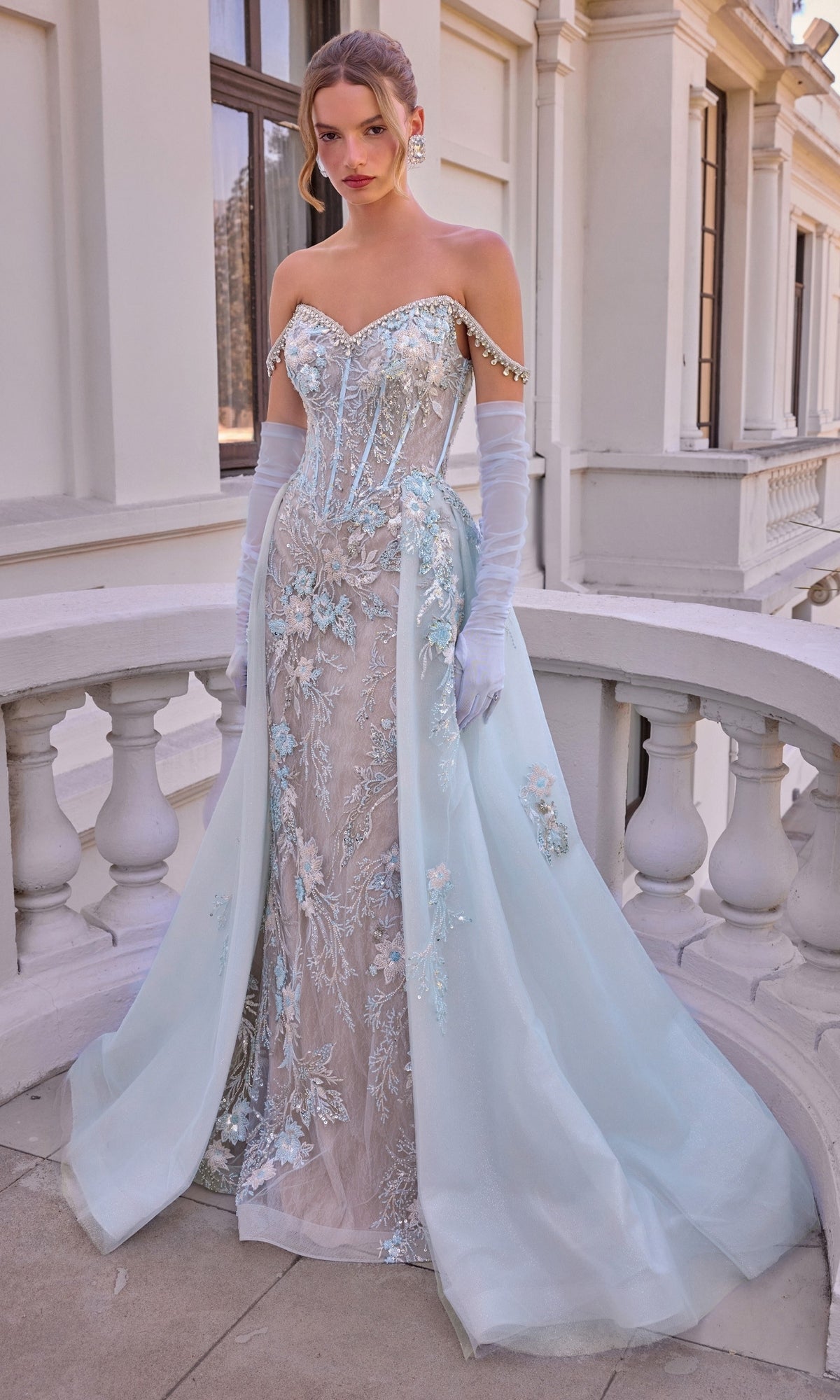 Ethereal Blue Prom Dress: Andrea & Leo A1518, an off-the-shoulder light blue gown with a sheer corset bodice, embellished floral embroidery, an overskirt, and matching sheer opera gloves.