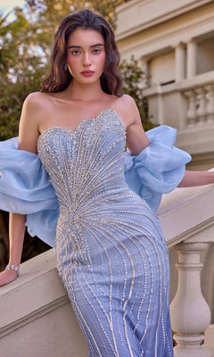 Wearing the Andrea & Leo A1519, a long light blue beaded prom dress with a strapless sweetheart neckline and sheer puff sleeves, a woman stands by a cream-colored staircase outdoors.
