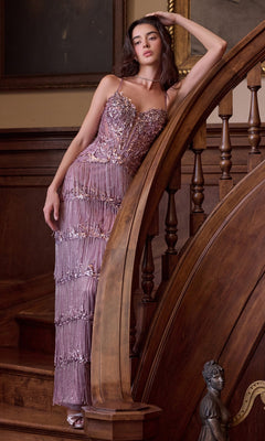 A model leans against a wooden staircase banister wearing the Vintage-Inspired Prom Dress: Andrea & Leo A1528, a mauve, floor-length gown with a sparkly, embellished corset bodice and a fringed skirt.