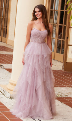 A woman stands outside near large windows and tiled floors, wearing the Nox Anabel A1591 Long Prom Dress—a strapless corset gown with a ruffled A-line skirt and sparkling embellishments.
