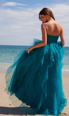 Wearing the Nox Anabel A1591 long prom dress with a glitter tulle ruffled A-line skirt, a woman stands on a sandy beach, gazing at the ocean beneath a partly cloudy sky.