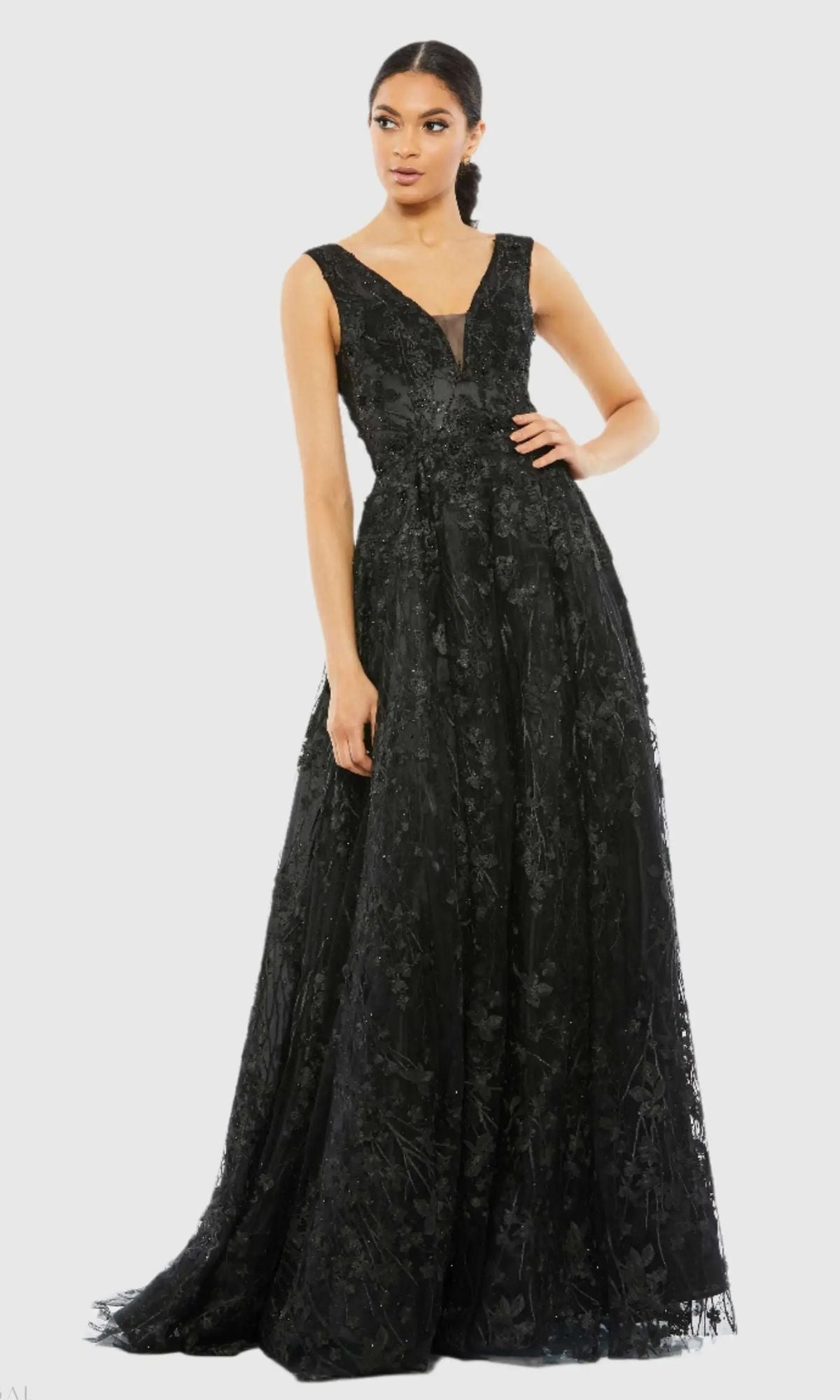 A woman wears the Mac Duggal A20131 Embroidered Long Formal Dress, a sleeveless black gown with a V-neckline and textured floral details, standing against a plain light background.