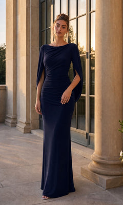 Woman in a navy Betsy & Adam A23033 long formal dress with elegant cape sleeves stands on a stone terrace in front of tall windows and columns at sunset.