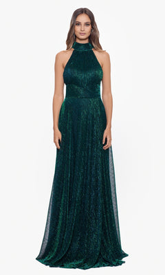 A woman faces forward, wearing the Empire-Waist High-Neck Long Shimmer Prom Dress A24948, a sleeveless, floor-length gown in dark green with textured, shimmering fabric.