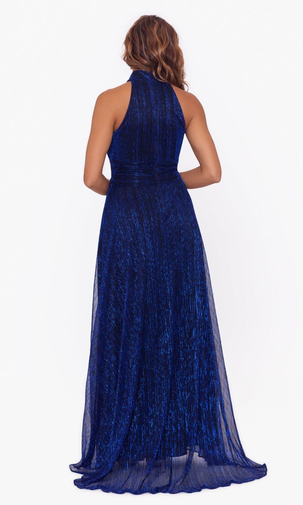 A woman stands with her back to the camera, wearing the Empire-Waist High-Neck Long Shimmer Prom Dress A24948 in dark blue with a textured gown and sheer overlay, set against a plain white background.