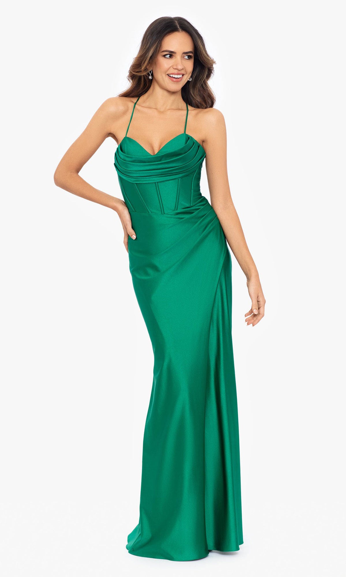 A woman poses against a plain white background wearing the Betsy and Adam Long Green Prom Dress A25610, a floor-length, sleeveless emerald gown featuring thin straps and a corset-style bodice.