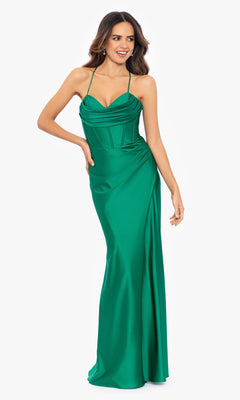 A woman poses against a plain white background wearing the Betsy and Adam Long Green Prom Dress A25610, a floor-length, sleeveless emerald gown featuring thin straps and a corset-style bodice.