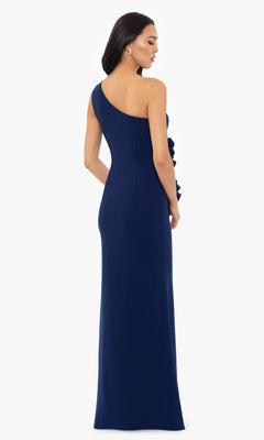 A woman stands facing away, showcasing the elegant back of the Betsy and Adam One-Shoulder Long Prom Dress A26071 in navy blue against a plain background.