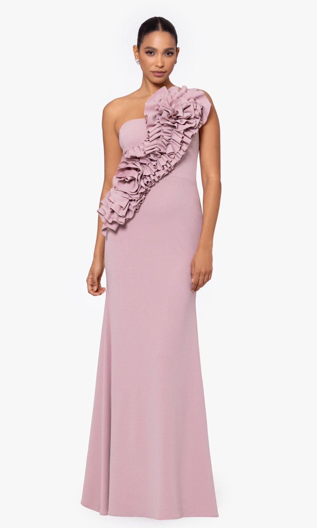 A woman models the Betsy and Adam One-Shoulder Long Prom Dress A26071 in mauve, featuring a floor-length silhouette and bold front ruffle detailing, standing against a plain white background.
