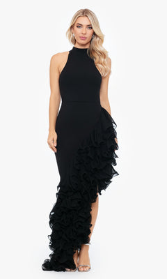 A woman wears the Betsy and Adam Long Black Ruffled Prom Dress A26173, featuring a high neckline and dramatic ruffled detailing on one side, paired with metallic open-toe heels.