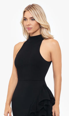 A woman with blonde hair models the Betsy and Adam Long Black Ruffled Prom Dress A26173, a sleeveless high-neck gown, against a plain white background.