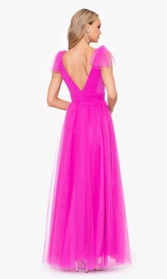 A woman faces away, wearing the Betsy & Adam Shoulder-Bow Long Prom Dress A26256 in bright pink, featuring a dramatic deep V-back, tulle cap sleeves, and a flowing A-line silhouette.