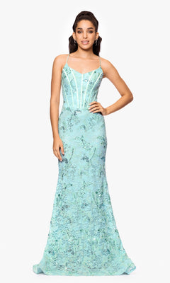 A woman stands facing forward in the Betsy and Adam A26885, a sleeveless, floor-length light blue lace formal dress with floral patterns and thin straps, against a plain white background.