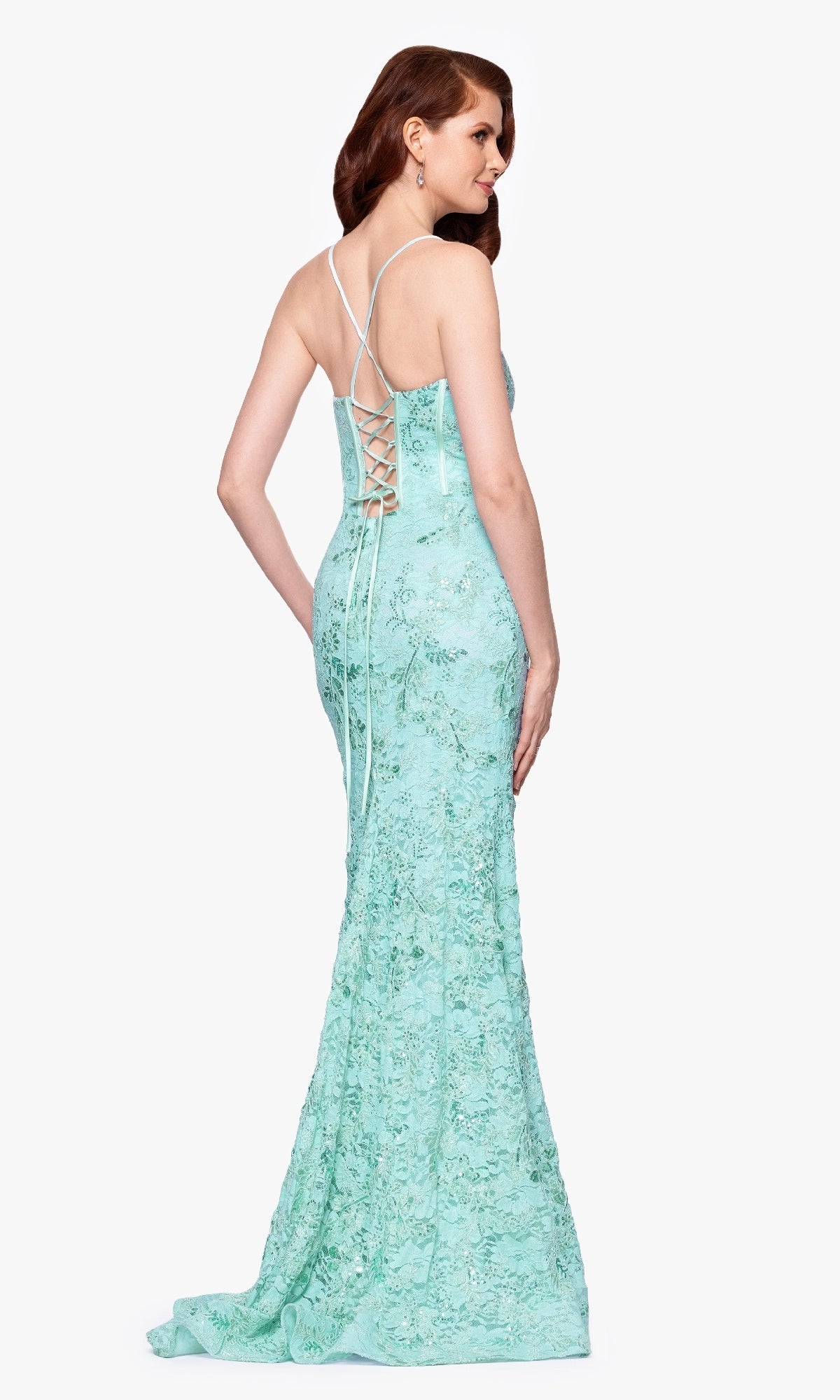 Woman wearing the Betsy and Adam A26885 long formal dress in light blue lace, featuring a fitted corset bodice, lace-up back, and thin straps, standing and facing slightly away.