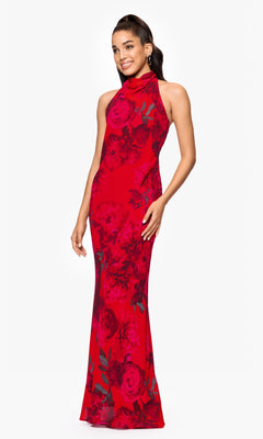 A woman smiles while standing against a white background, wearing the Betsy & Adam A26926 Long Red Floral Formal Dress—a sleeveless, floor-length gown with a high neckline.