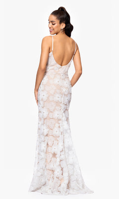 Woman in the Betsy and Adam A26948 long formal dress, fitted white with floral pattern, delicate lace, and adjustable straps, faces away and looks over her shoulder against a plain white background.