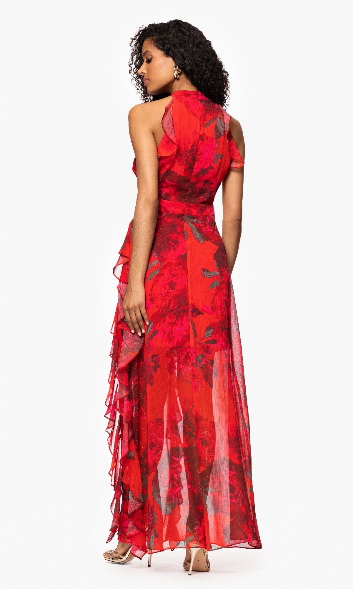 A woman stands with her back to the camera against a white background, wearing the Betsy and Adam A26962 Floral-Print Red Formal Dress, a sleeveless, floor-length gown with ruffle details.