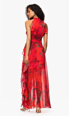 A woman stands with her back to the camera against a white background, wearing the Betsy and Adam A26962 Floral-Print Red Formal Dress, a sleeveless, floor-length gown with ruffle details.