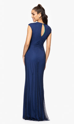 Model wears the Betsy and Adam A26963 long formal dress in navy, featuring a fitted, floor-length design with a small back keyhole detail. She faces away, smiling over her shoulder against a plain white background.
